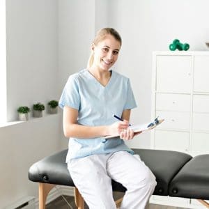 Profesional de la salud o fisioterapeuta con uniforme azul y portapapeles en una sala de tratamiento privada de lujo.